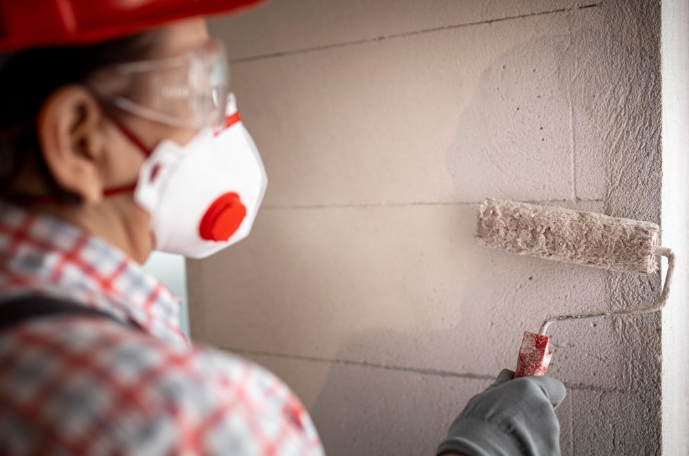 Person wearing a respirator and safety glasses paints a wall with a roller