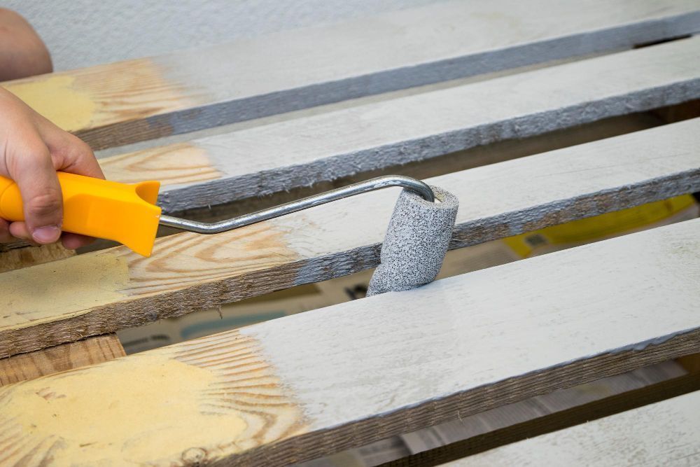 Hand sanding a wooden surface with a yellow sanding tool and gray sanding block