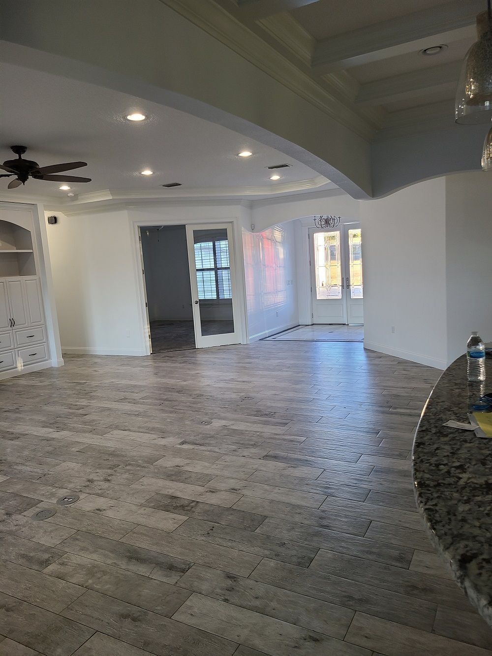 Spacious empty living room with gray patterned tile floor, white walls, ceiling fan, and large windows.