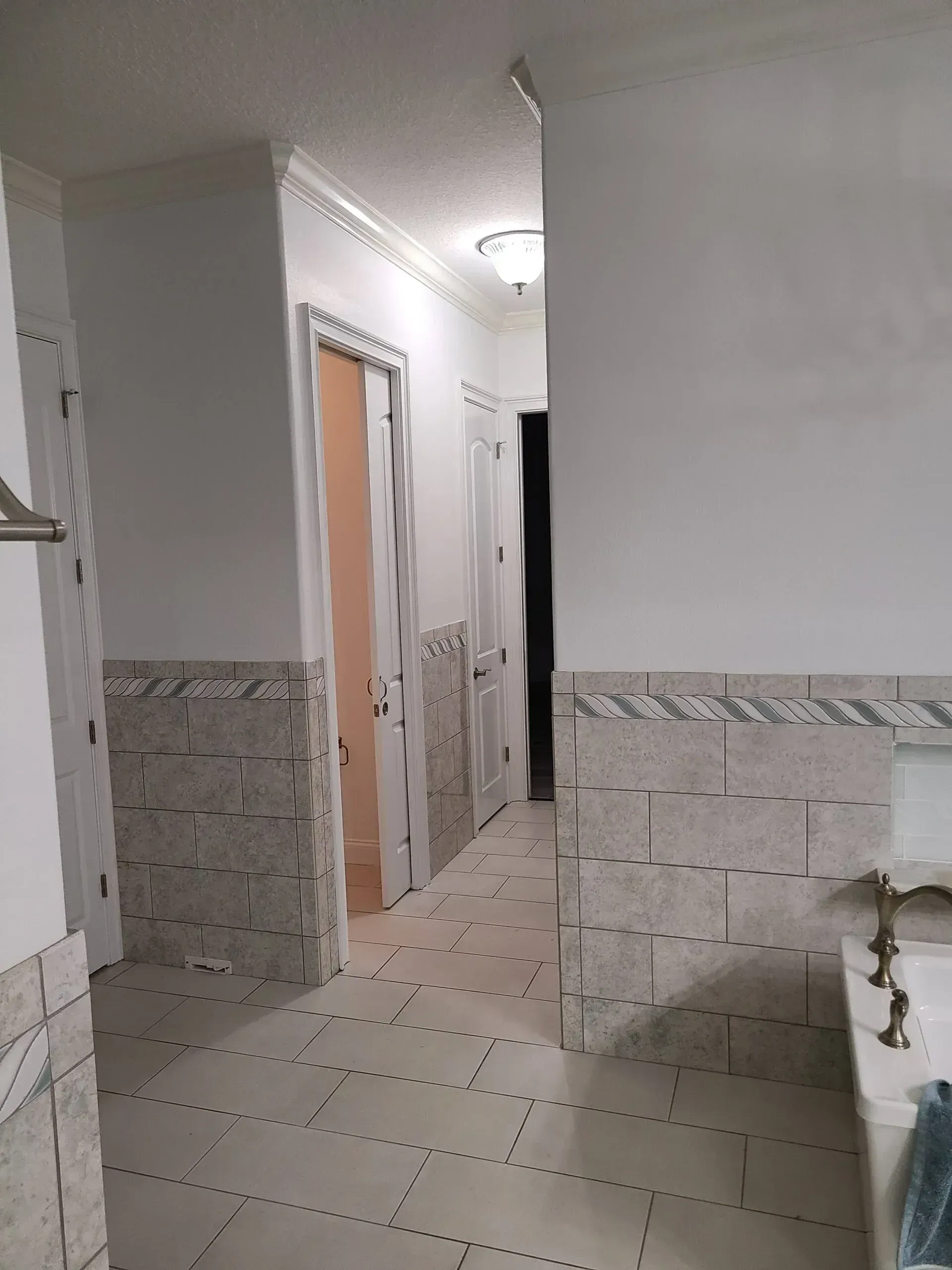 Narrow tiled hallway with doors, white walls, and a ceiling light in an apartment or hotel interior
