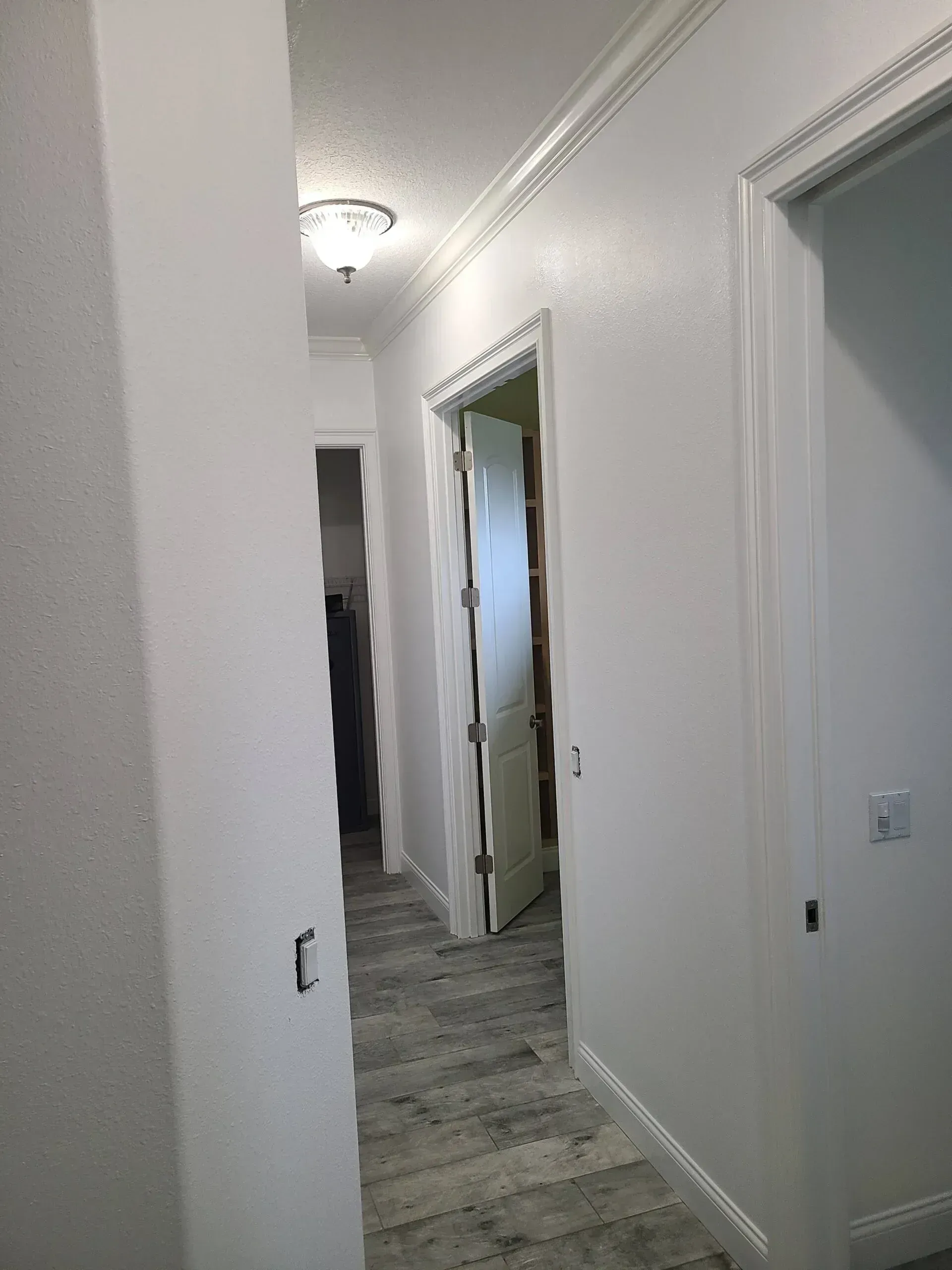 Narrow white hallway with open doorways and gray tile flooring in a home