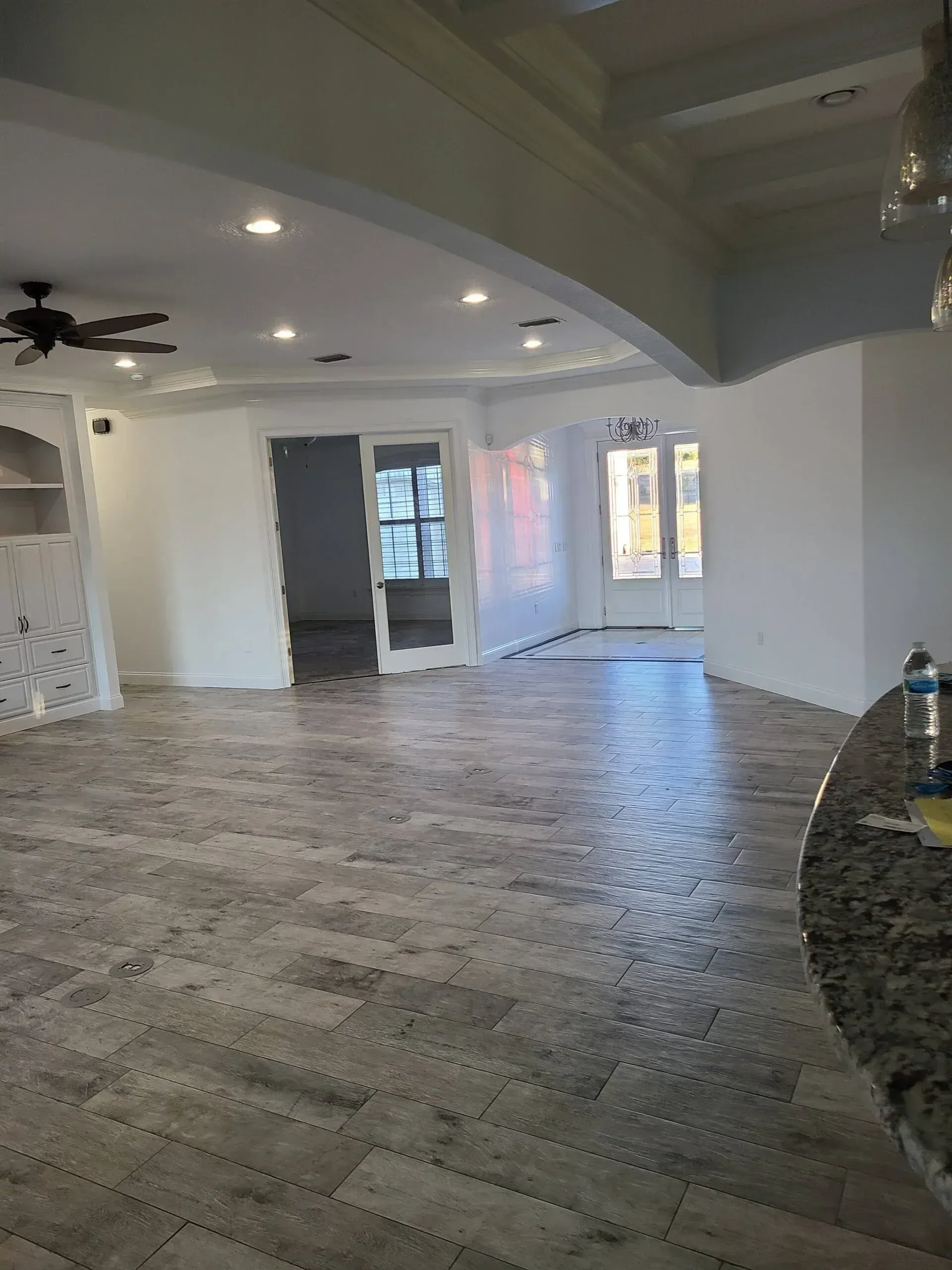 Empty open-plan room with gray wood floors, white walls, recessed lighting, and a ceiling fan