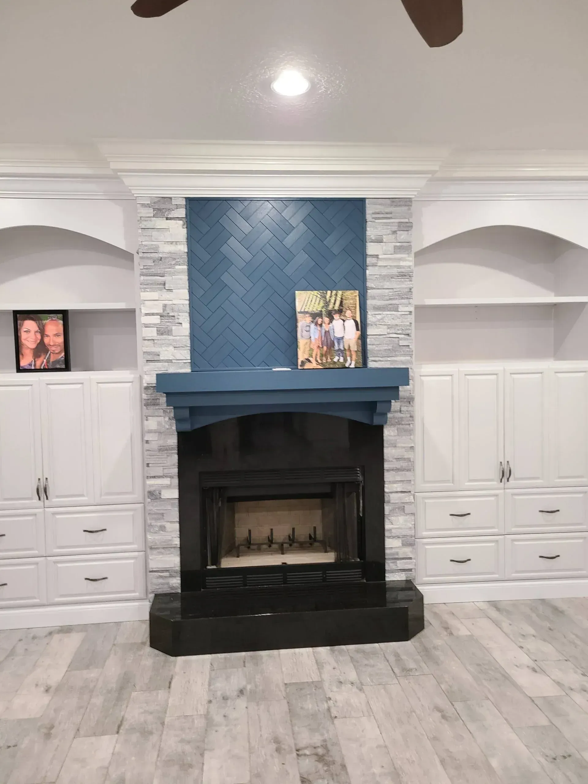 Living room with a blue-tiled fireplace, white built-in cabinets, and light wood flooring