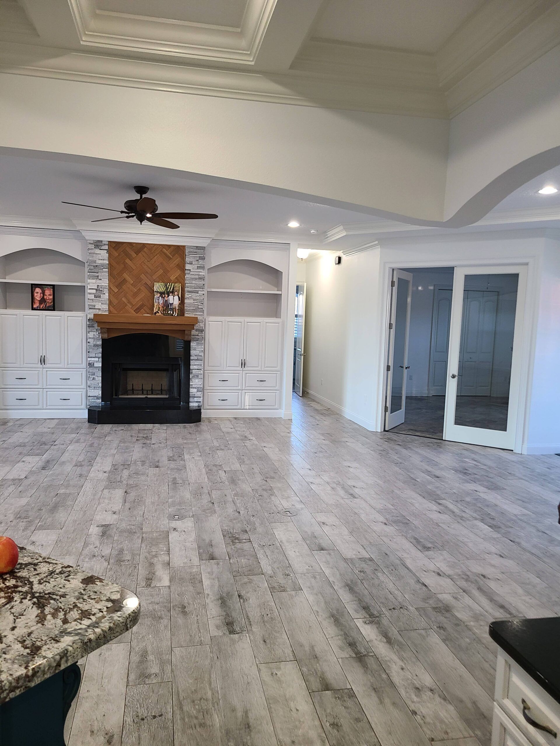 Spacious living room with gray floors, white walls, a fireplace, ceiling fan, and French doors