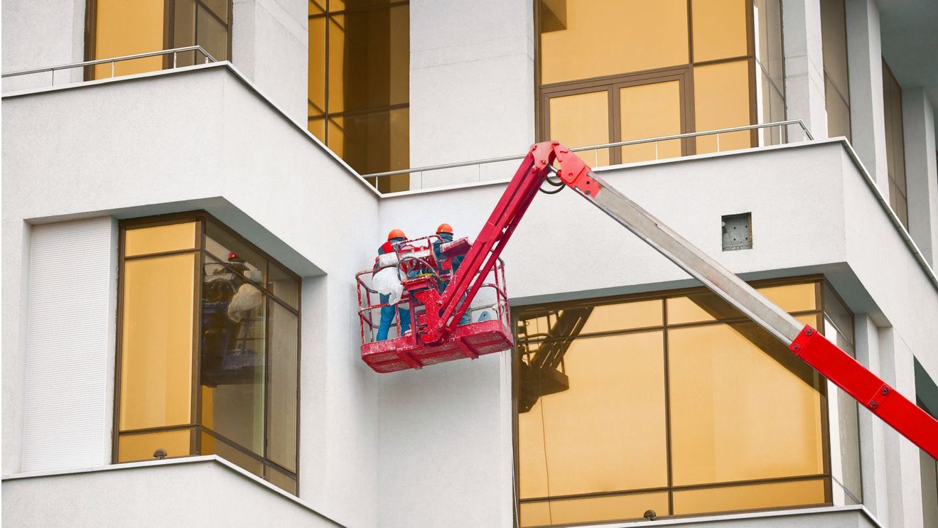 Workers in a red cherry picker washing a white building’s windows and facade