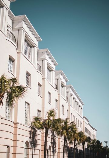 Beige multi-story building with white trim under a clear blue sky, palm trees in front.