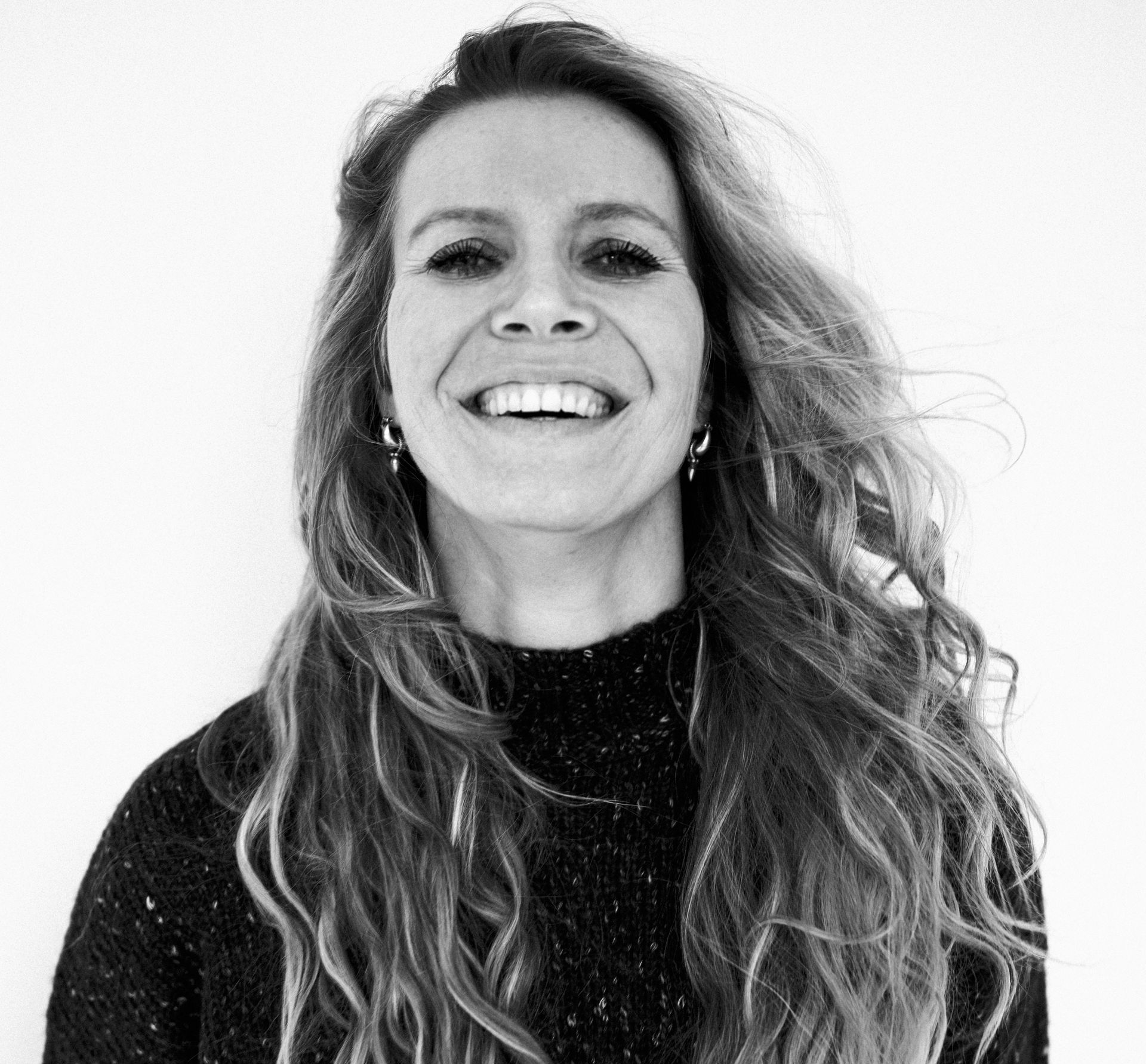 Debbie lacht breed, gekleed in een donkere trui, tegen een witte achtergrond.
