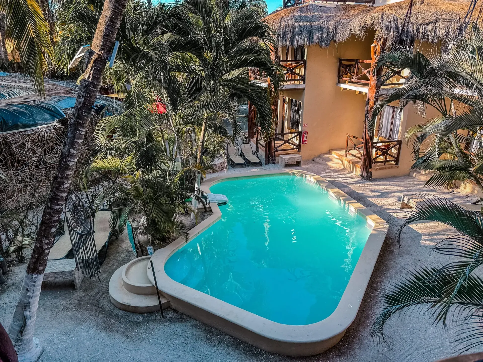 Piscina y edificio bronceado rodeado de árboles; resort tropical.