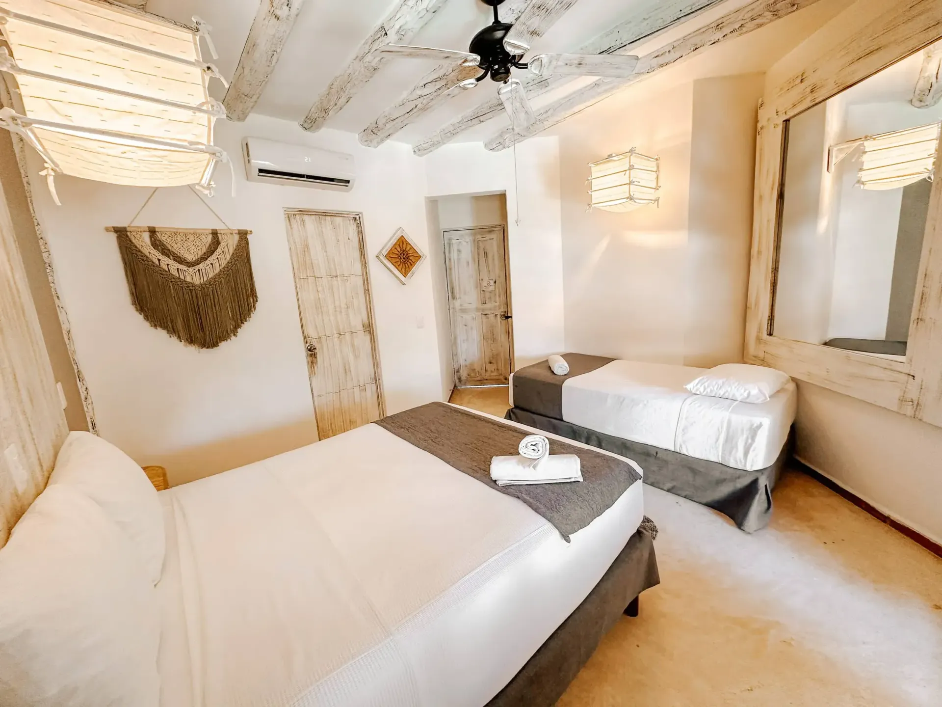 Dormitorio con dos camas, paredes blancas, iluminación decorativa y puerta de entrada.