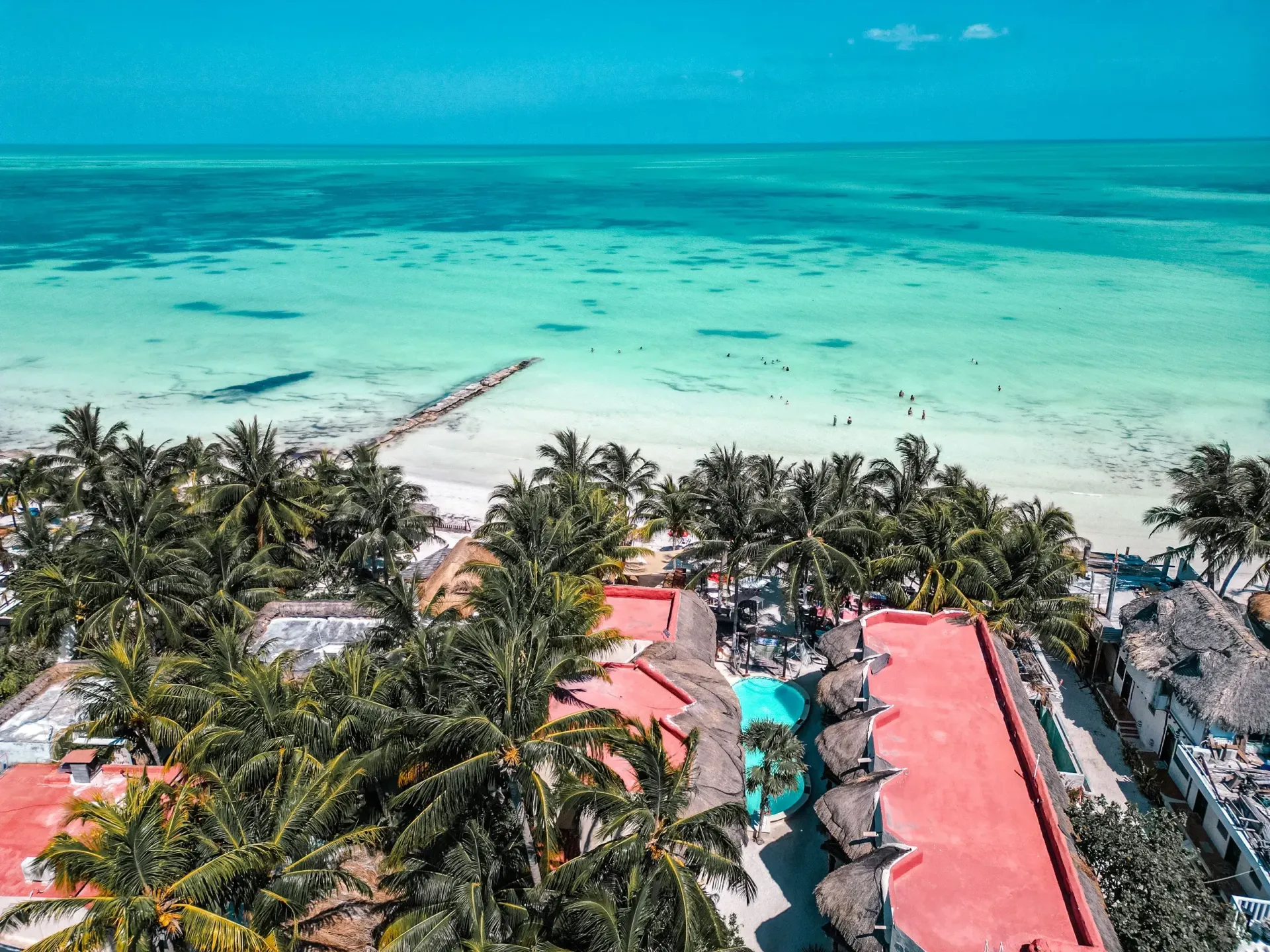 Balneario tropical con palmeras, aguas turquesas y edificios con tejados rojos.