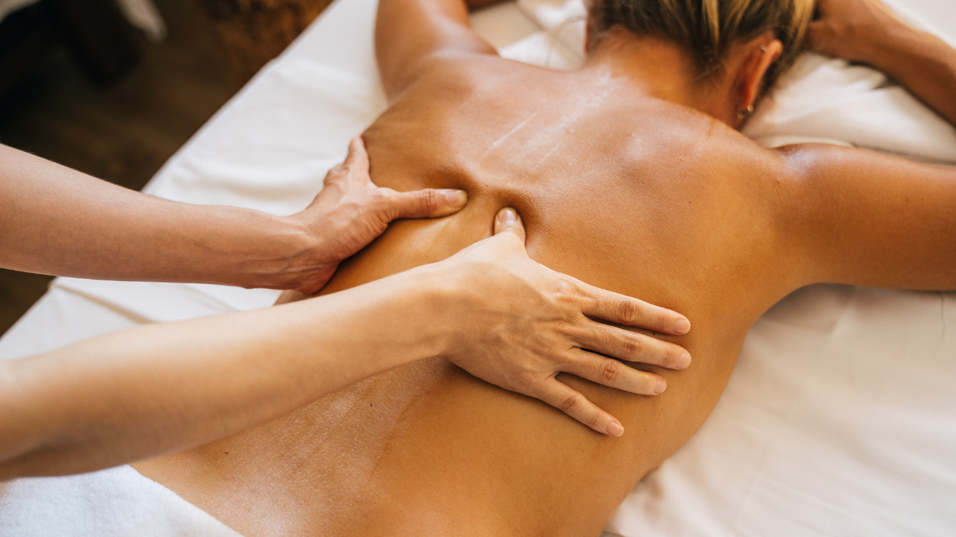 Hands giving a back massage on a person lying face down on a massage table.