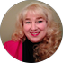 Woman with blonde curly hair smiles, wearing a pink blazer and black top.