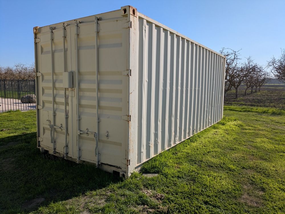 Beige shipping container on a grassy field under a clear blue sky.