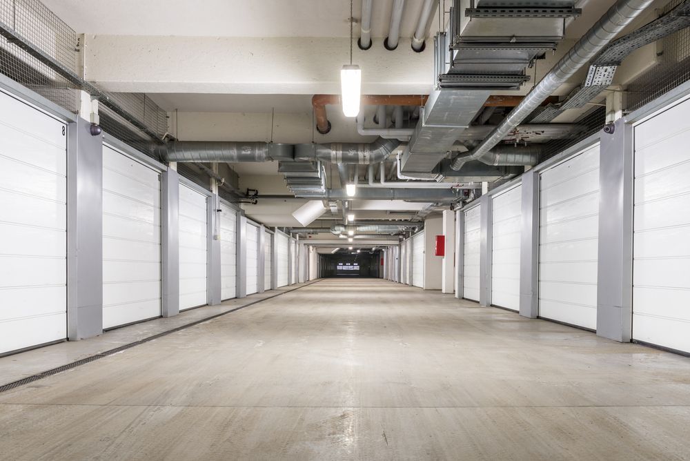 Long hallway with storage units on either side; ceiling pipes and lighting.