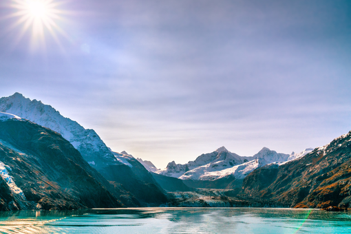 Snowy mountains above a turquoise alpine lake under a bright sun and clear sky