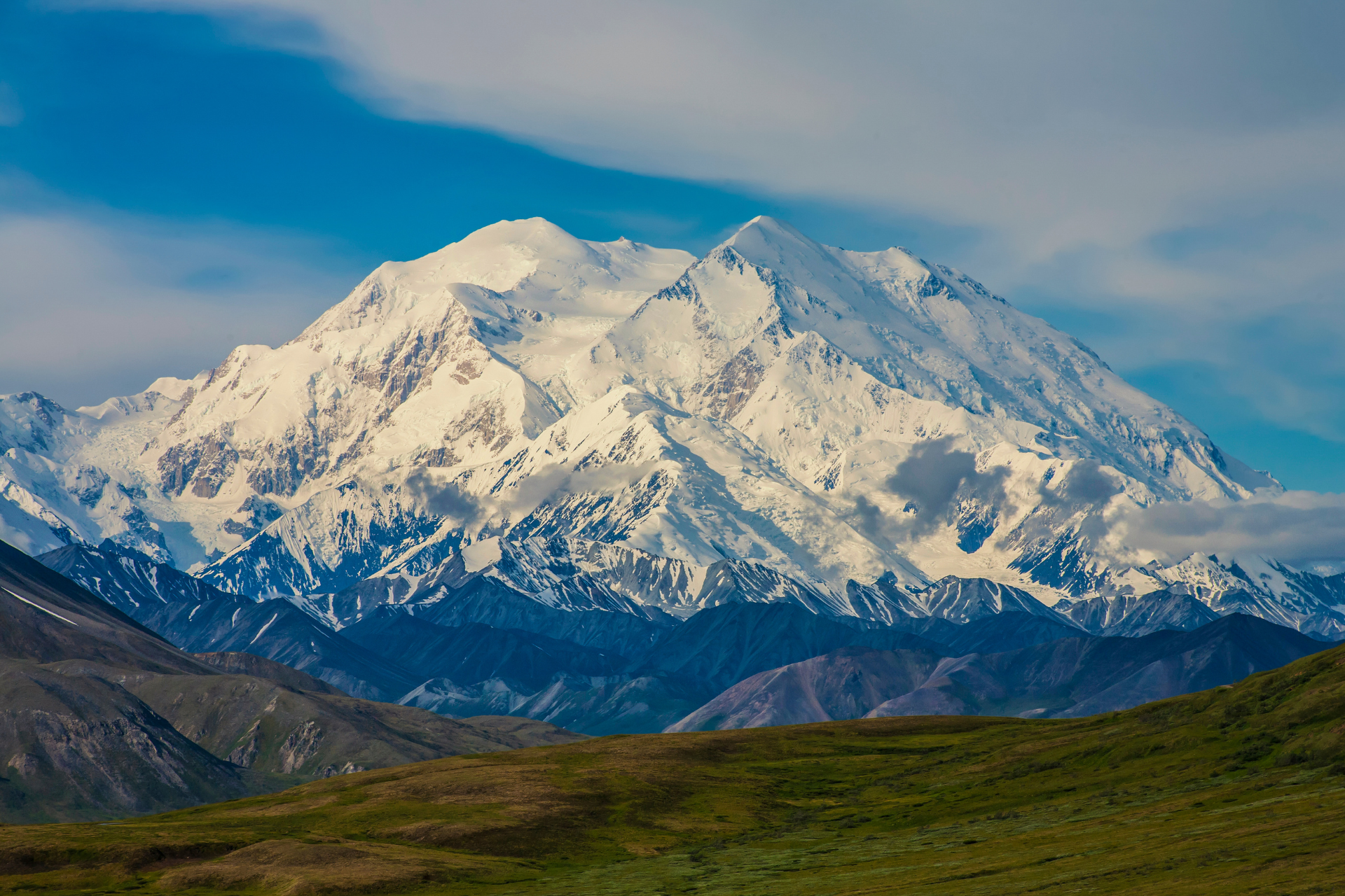 Snow-covered mountain under a clear blue sky, with green foothills in the foreground.