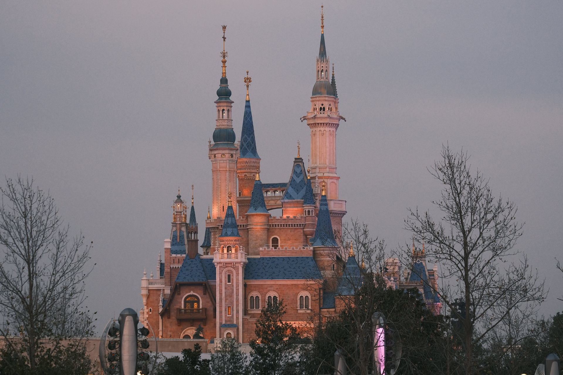 Fairy-tale castle with blue spires lit at dusk behind bare trees