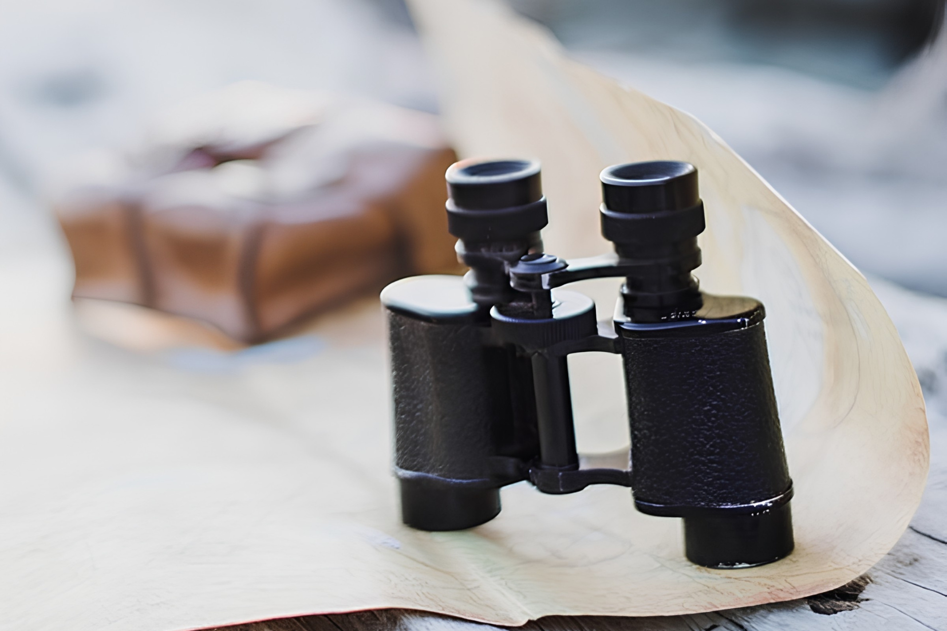 Black binoculars resting on a wooden surface beside a blurred beige hat