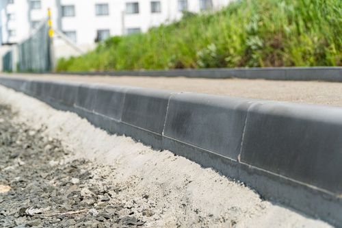 Close-up of a concrete curb edging a gravel path beside a landscaped sidewalk