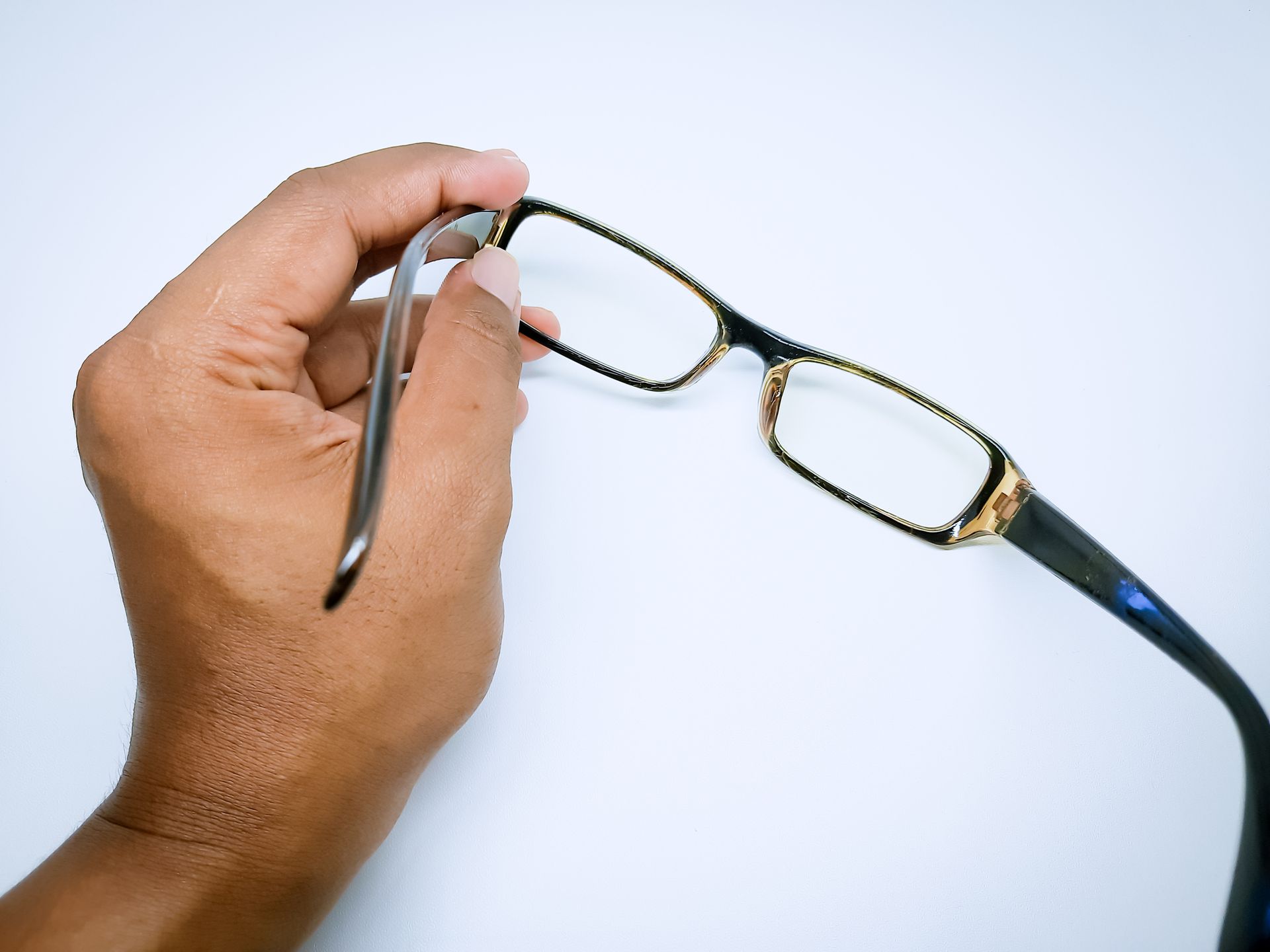 Hand holding black-framed eyeglasses on a light blue background