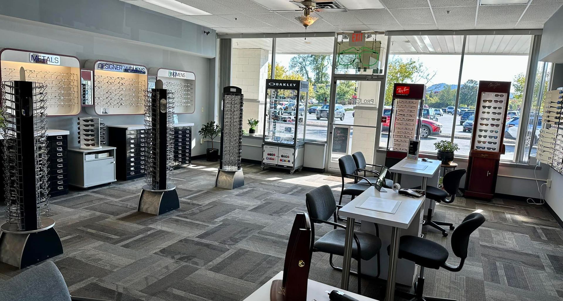 Bright eyeglass store interior with display stands, chairs, and desks near front windows