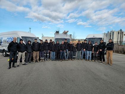 Group of workers standing in front of vans, likely an electrical company. 