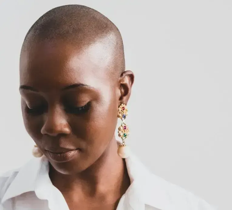 Portrait of a person with a shaved head wearing a white shirt and colorful dangling earrings, looking down