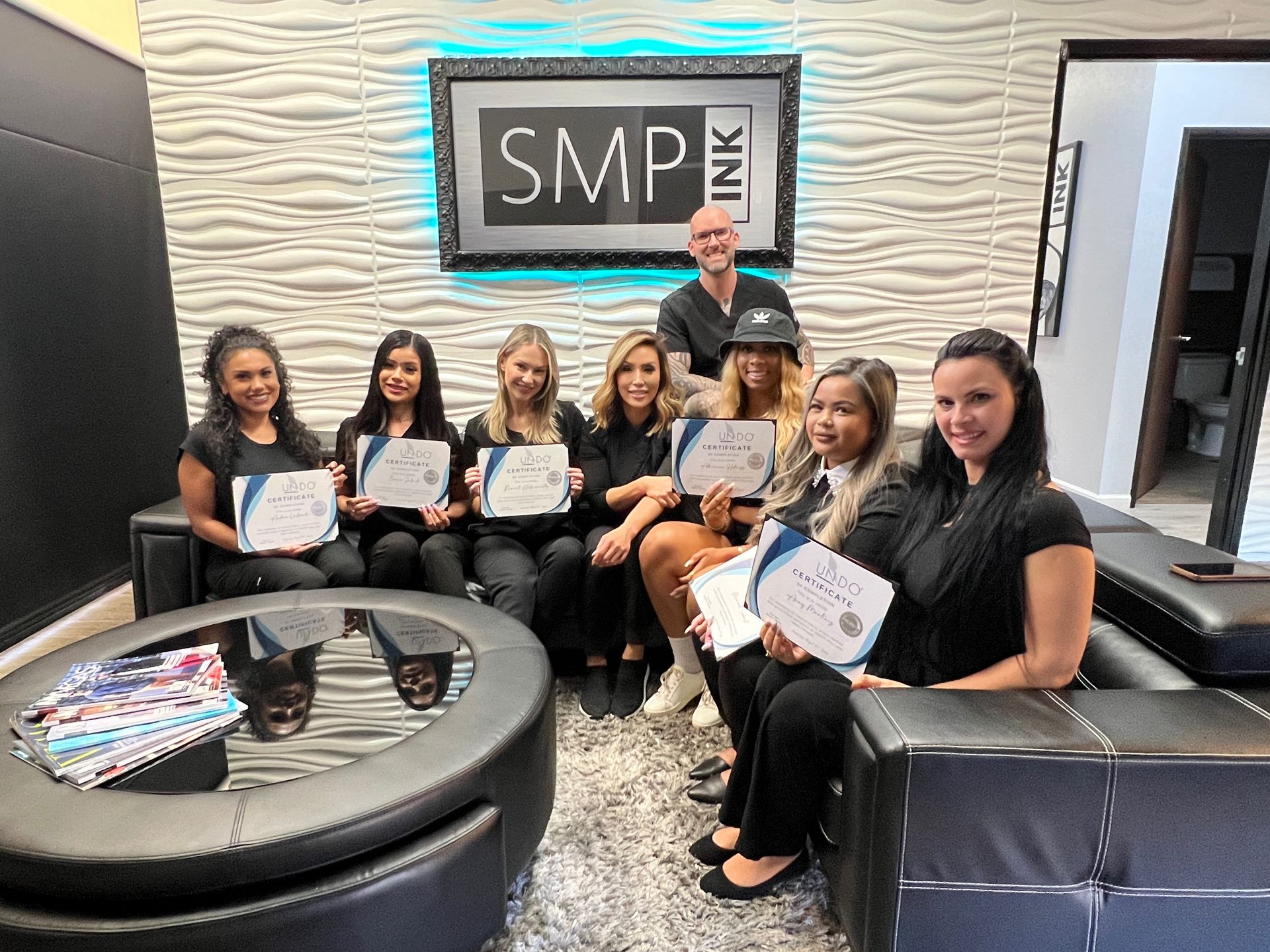 Group posing in a modern lounge, holding certificates with an SMP sign on the wall behind them.