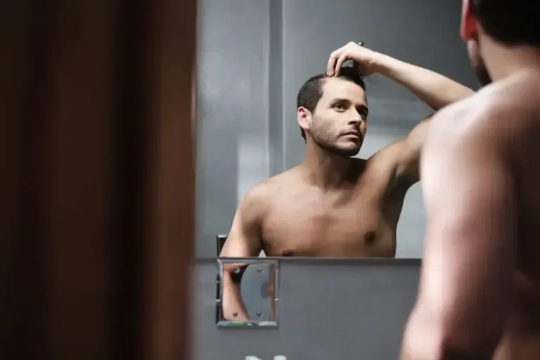 man looking at thinning hair in the mirror