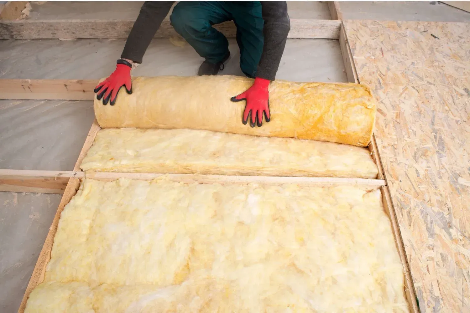 A man is rolling a roll of insulation on the floor.