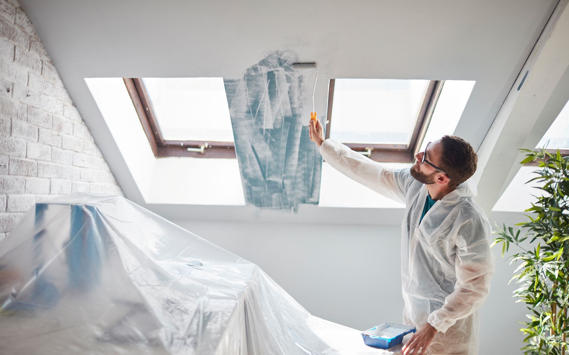 A man is painting the ceiling of a room.