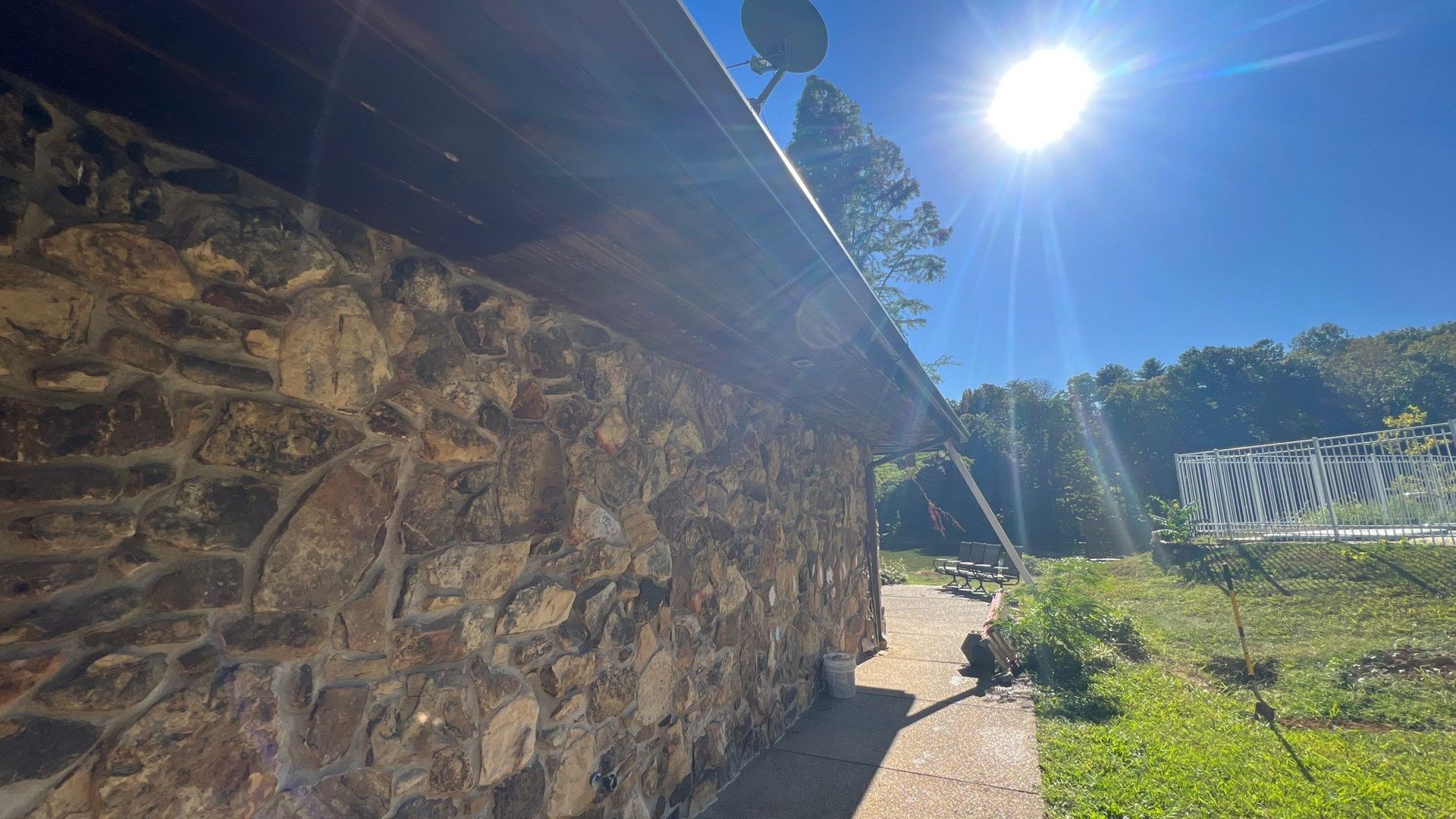 A stone wall with a gutter on it and the sun shining through it.