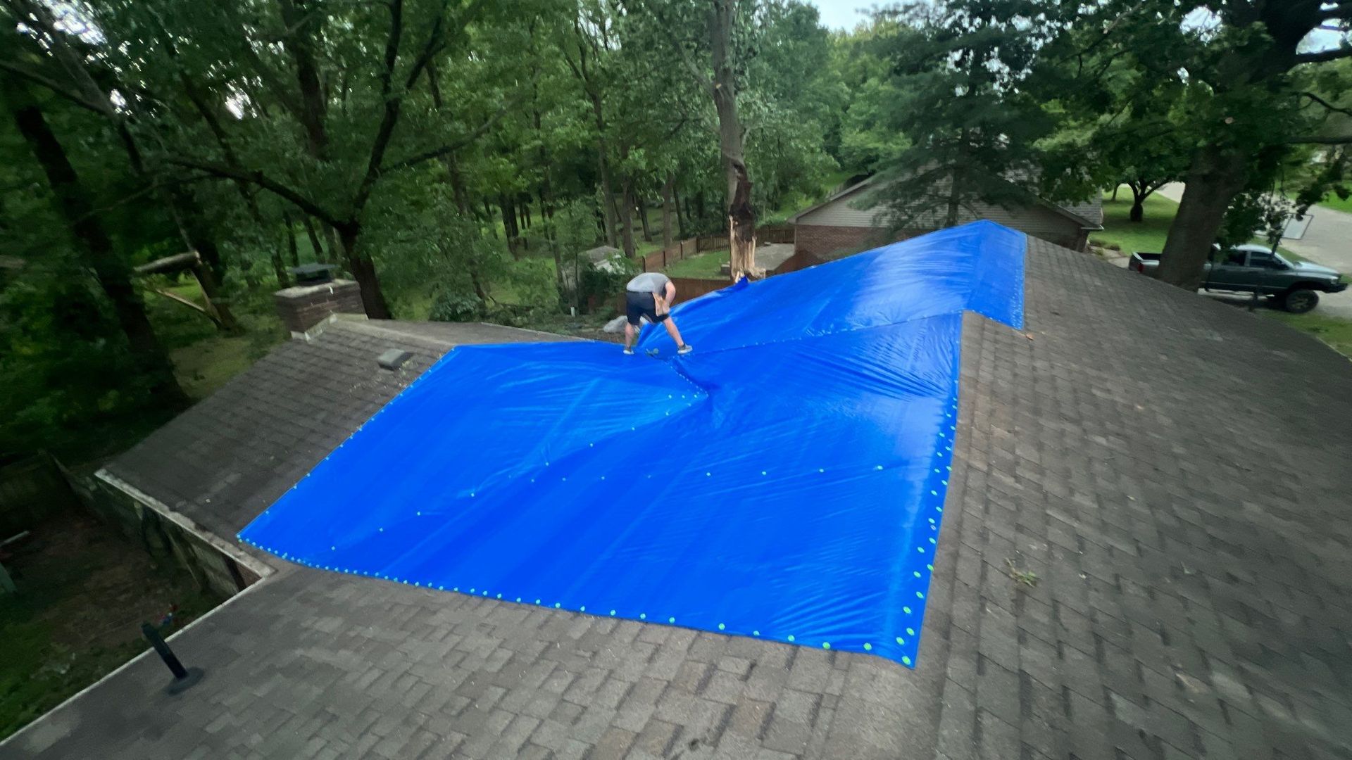 A person is standing on top of a roof with a blue tarp on it.