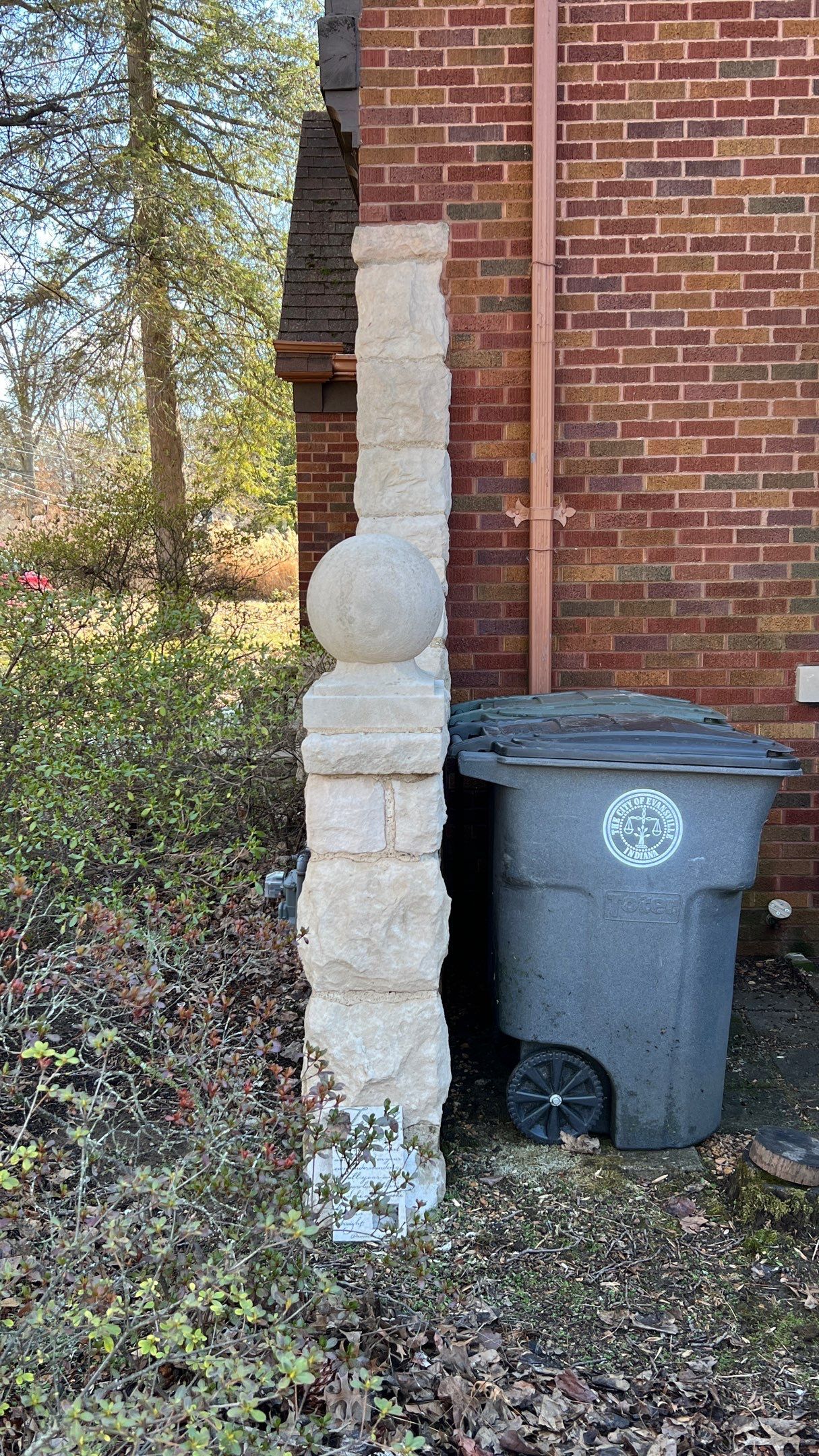 A trash can is sitting on the side of a brick building that has been cleaned.