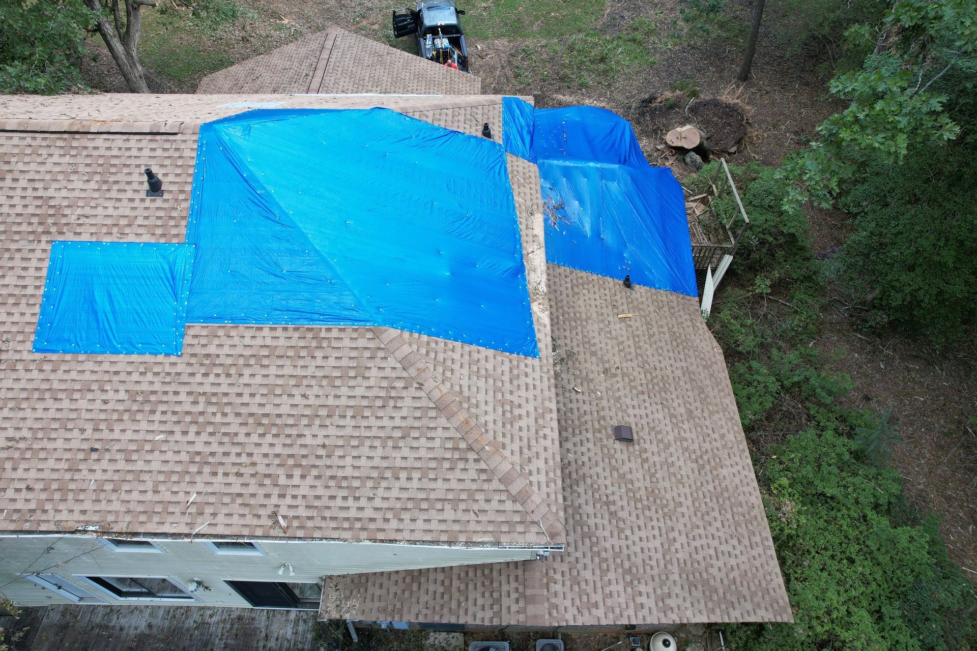 An aerial view of a house with a blue tarp on the roof.