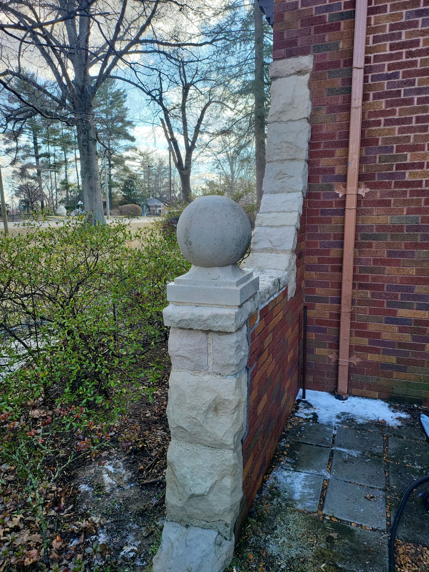 A stone pillar with a ball on top of it is next to a brick wall that has been cleaned.