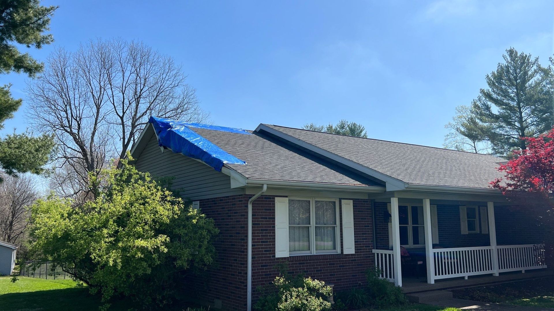 A brick house with a blue tarp on the roof.