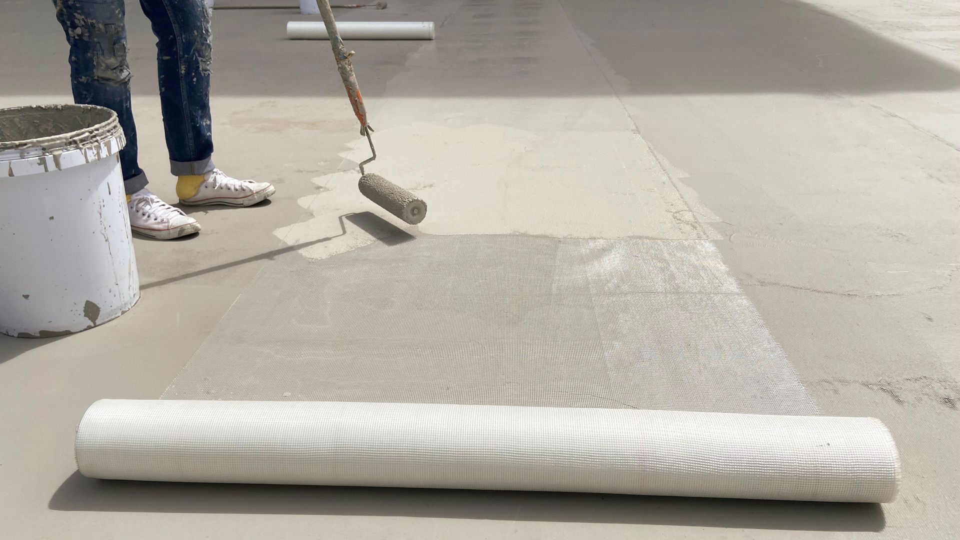 A person is painting a concrete floor with a roller.