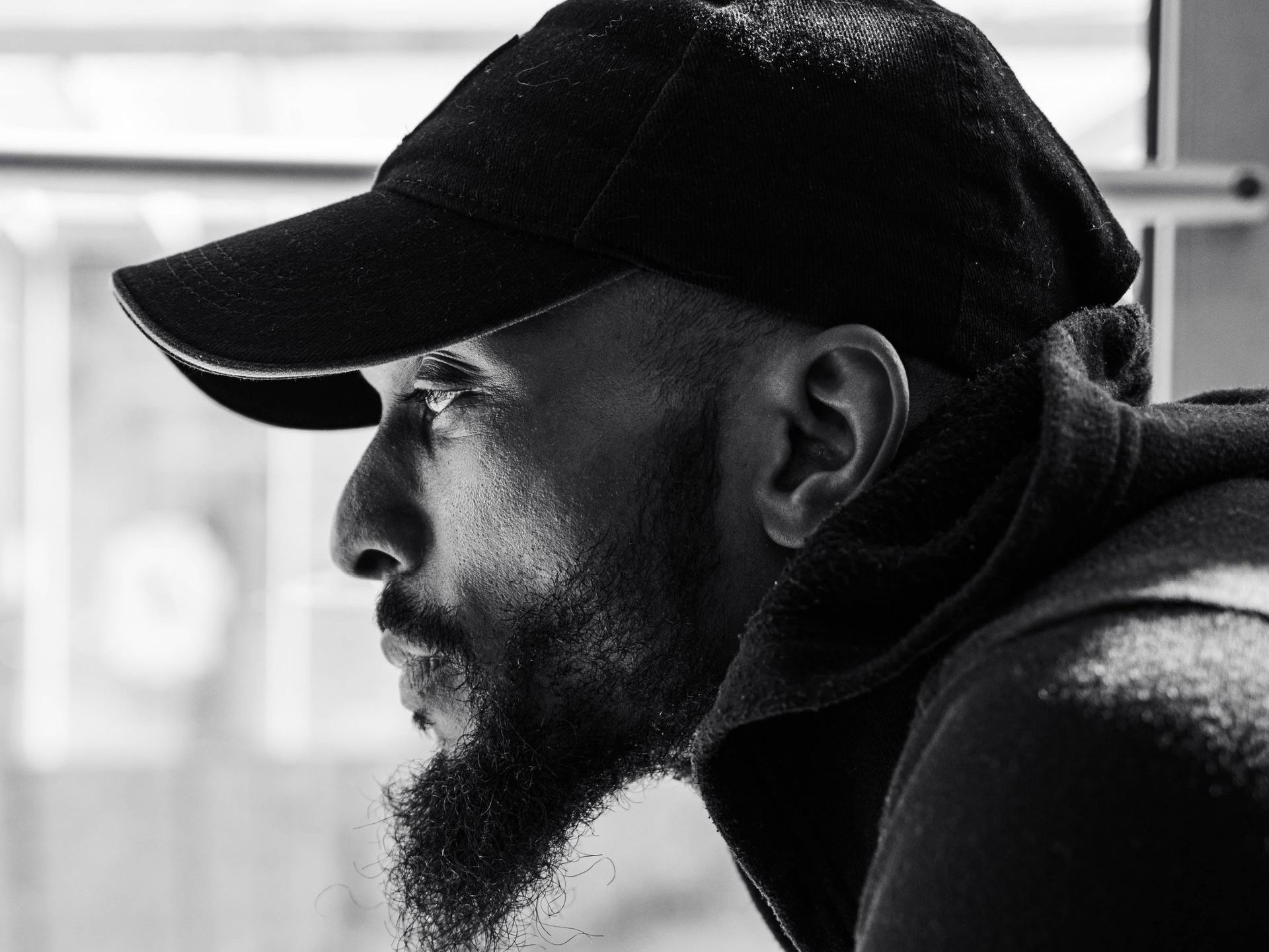 A black and white photo of a man with a beard wearing a baseball cap.