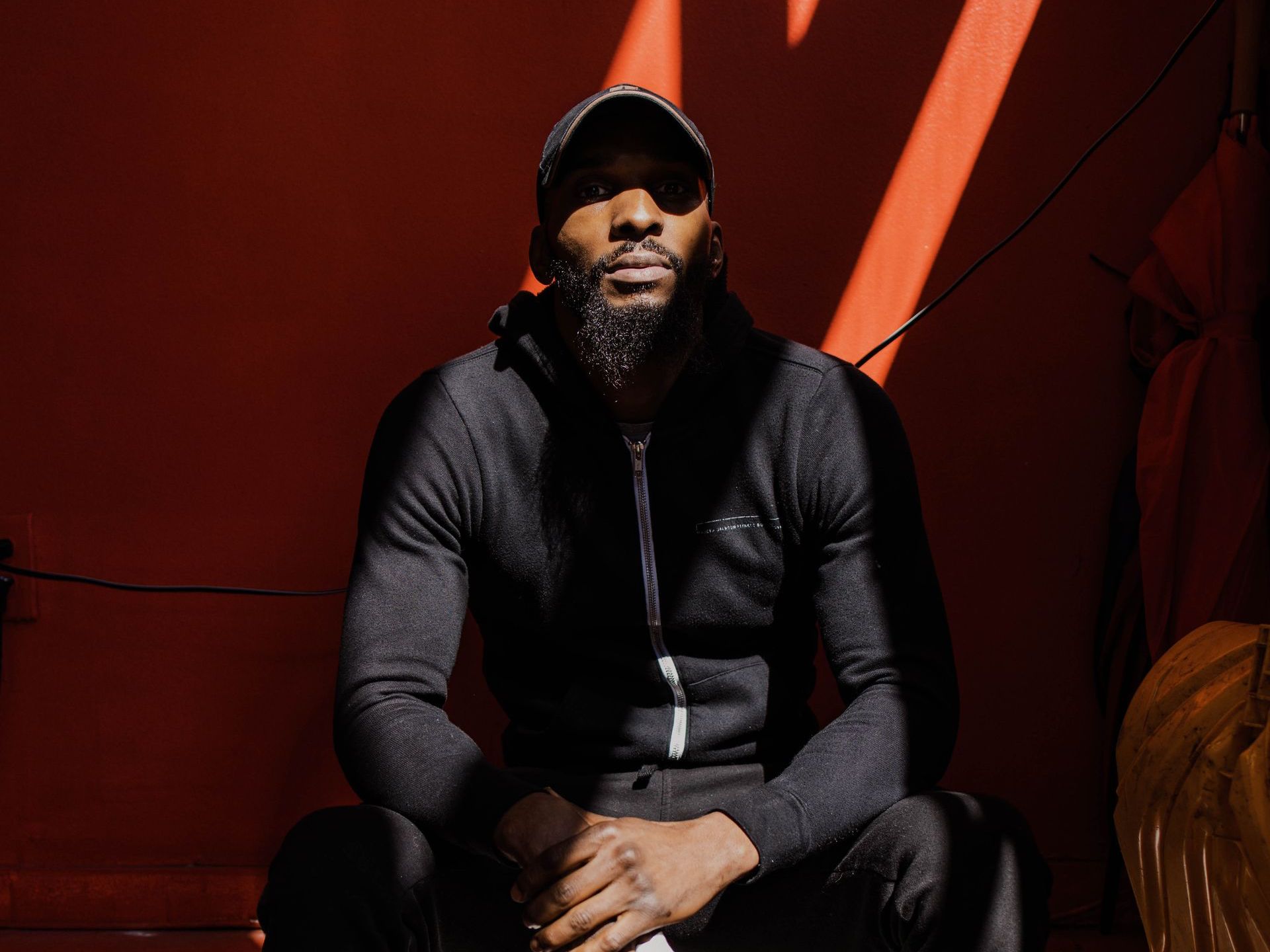 A man with a beard is sitting in front of a red wall.