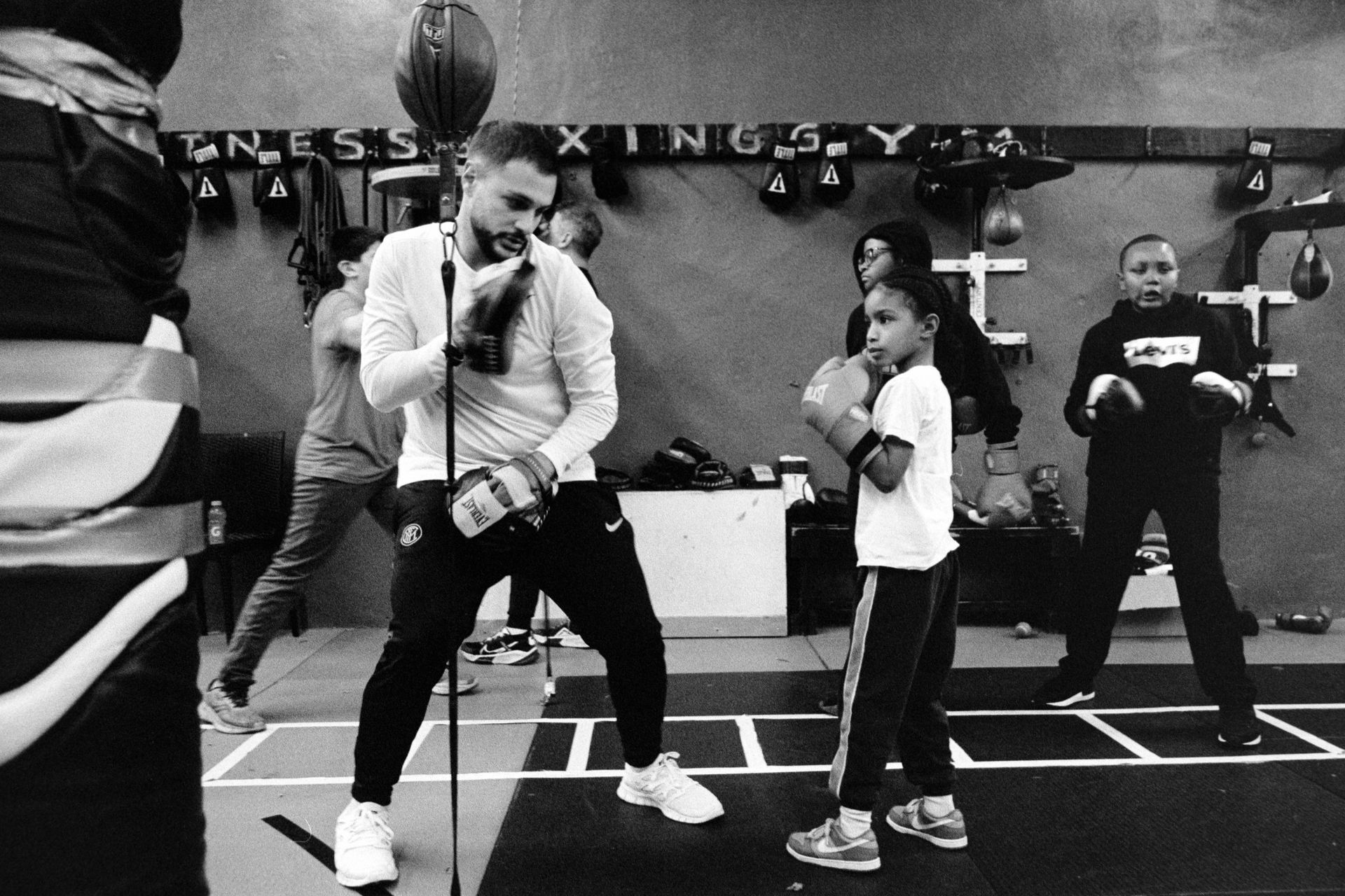 A man is singing into a microphone while a group of people are boxing in a gym.