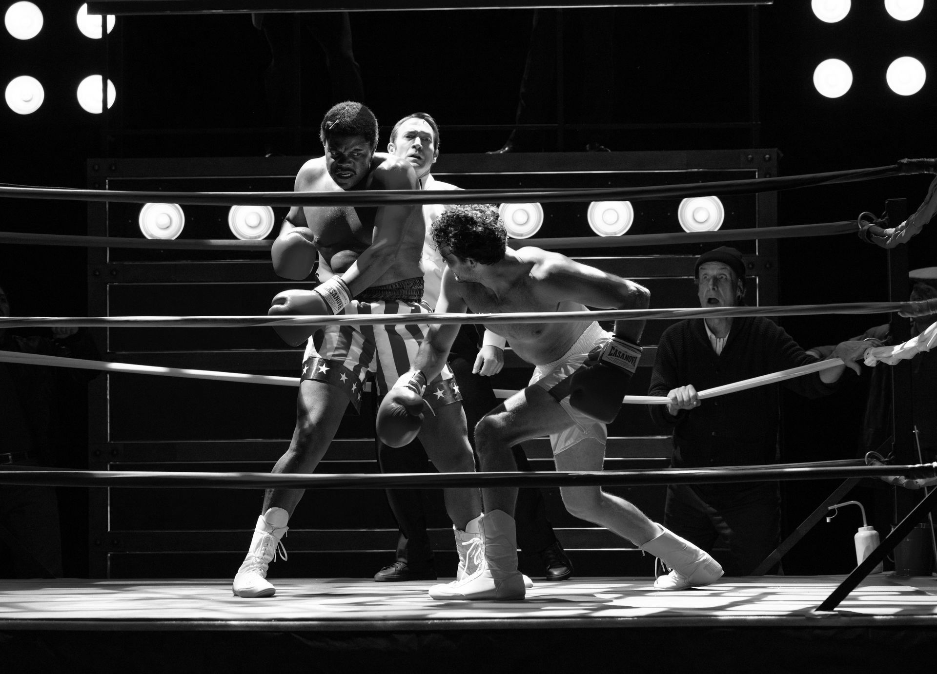 Two boxers are fighting in a boxing ring in a black and white photo.