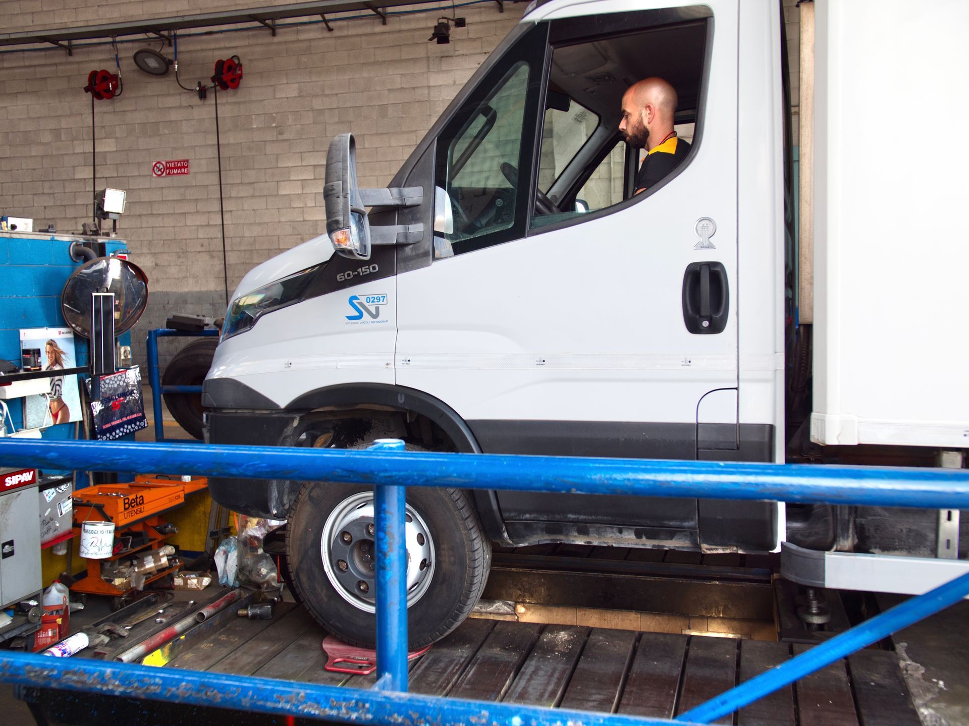 Camion bianco su una piattaforma di prova, autista al volante. Ambiente da garage.