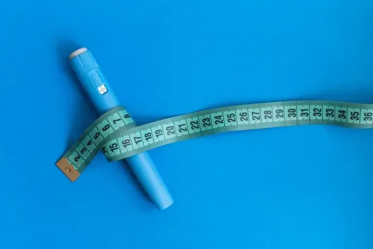 A blue pencil is wrapped in a measuring tape on a blue surface.