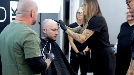 An SMP INK CDA Student Practitioner drawing the reference line on the scalp of an SMP client in a class setting.