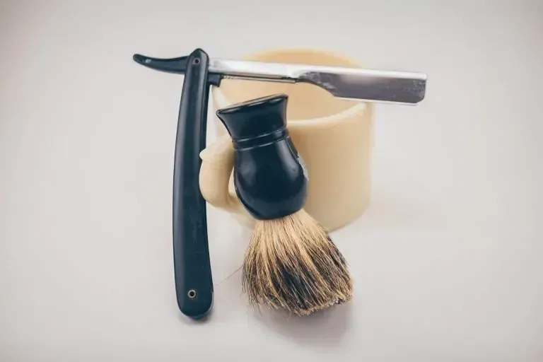 A razor and a shaving brush are sitting on top of a shaving mug.