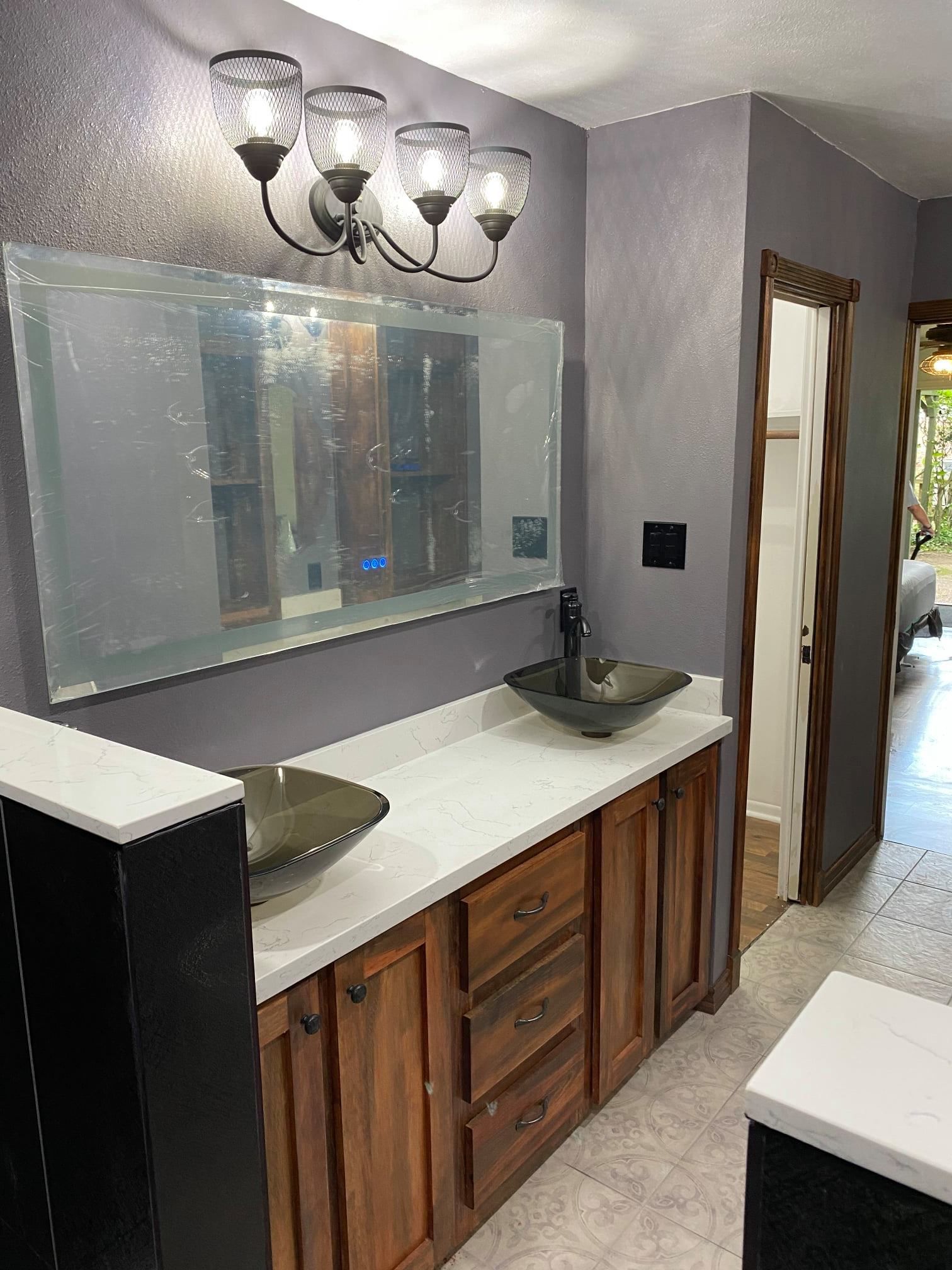 Bathroom vanity with double sinks, large mirror, and wall lights in a gray and wood-finished interior