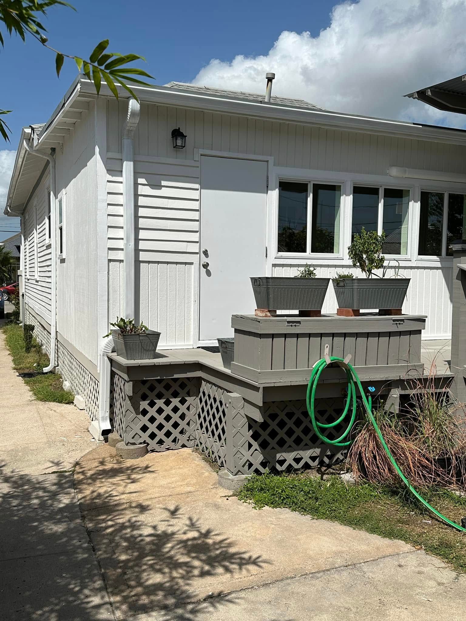 White house exterior with small wooden porch, lattice skirting, windows, and a green garden hose in the yard