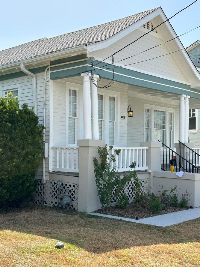 Small white house with porch, green trim, and black steps, seen from the front yard.