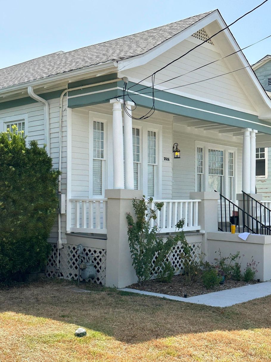 White bungalow-style house with a front porch, white trim, and black steps in a sunny yard